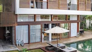 Ein modernes, zweistöckiges Haus mit Pool, Sitzgelegenheit im Freien und einem gepflegten Rasen.