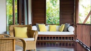 Ein Zimmer mit Holzterrasse, einer Couch mit Kissen und einem Korbstuhl.