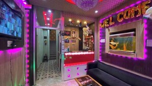 A reception area with a counter, a sofa, and a television. - Hotel Aditya (Varanasi)