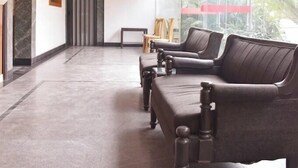A lobby with a seating area, marble flooring, ceiling fans, and a large window with a view of palm trees. - Hotel Aditya (Varanasi)