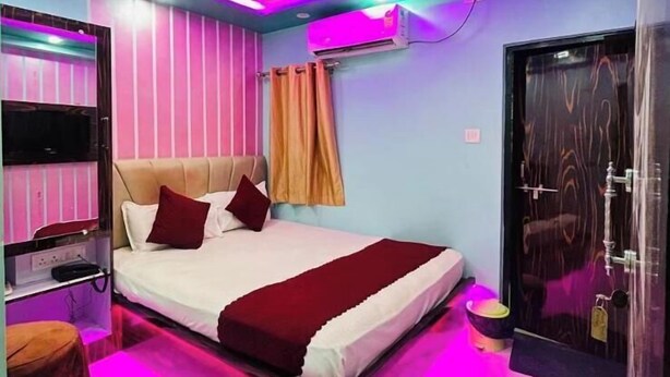 A modern bedroom with a bed, a TV, and a bathroom with a mirror and sink. - Hotel Aditya (Varanasi)