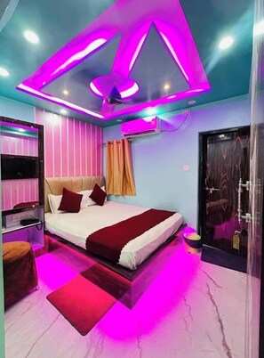 A modern bedroom with a bed, a TV, and a bathroom with a mirror and sink. - Hotel Aditya (Varanasi)