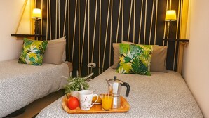 Habitación de hotel con dos camas, cada una con cubrecama estampado, una bandeja con cafetera, taza, manzana y vaso de zumo de naranja.