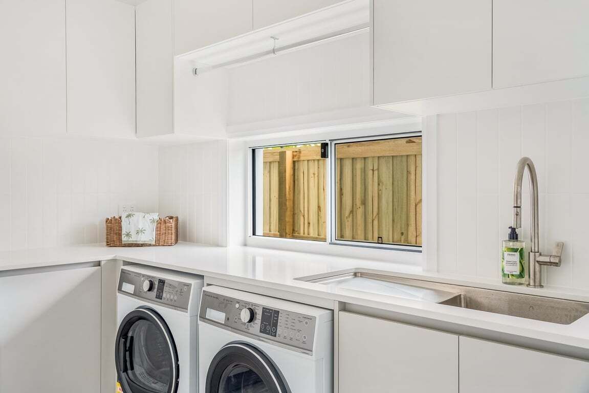 A modern kitchen with built-in appliances, a window with wooden shutters, and a stainless steel sink.
