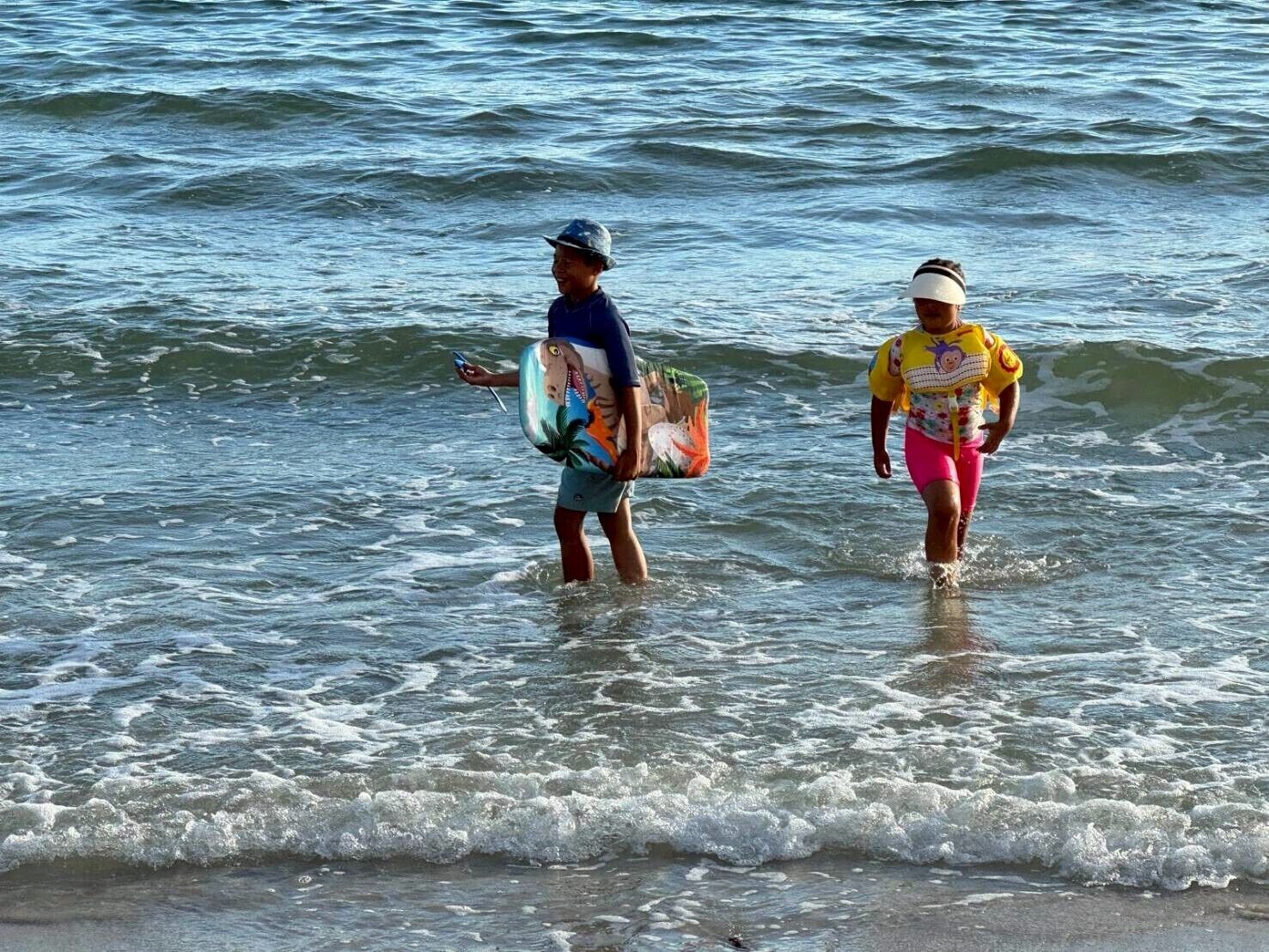 Dos personas caminando en aguas poco profundas cerca de la orilla.