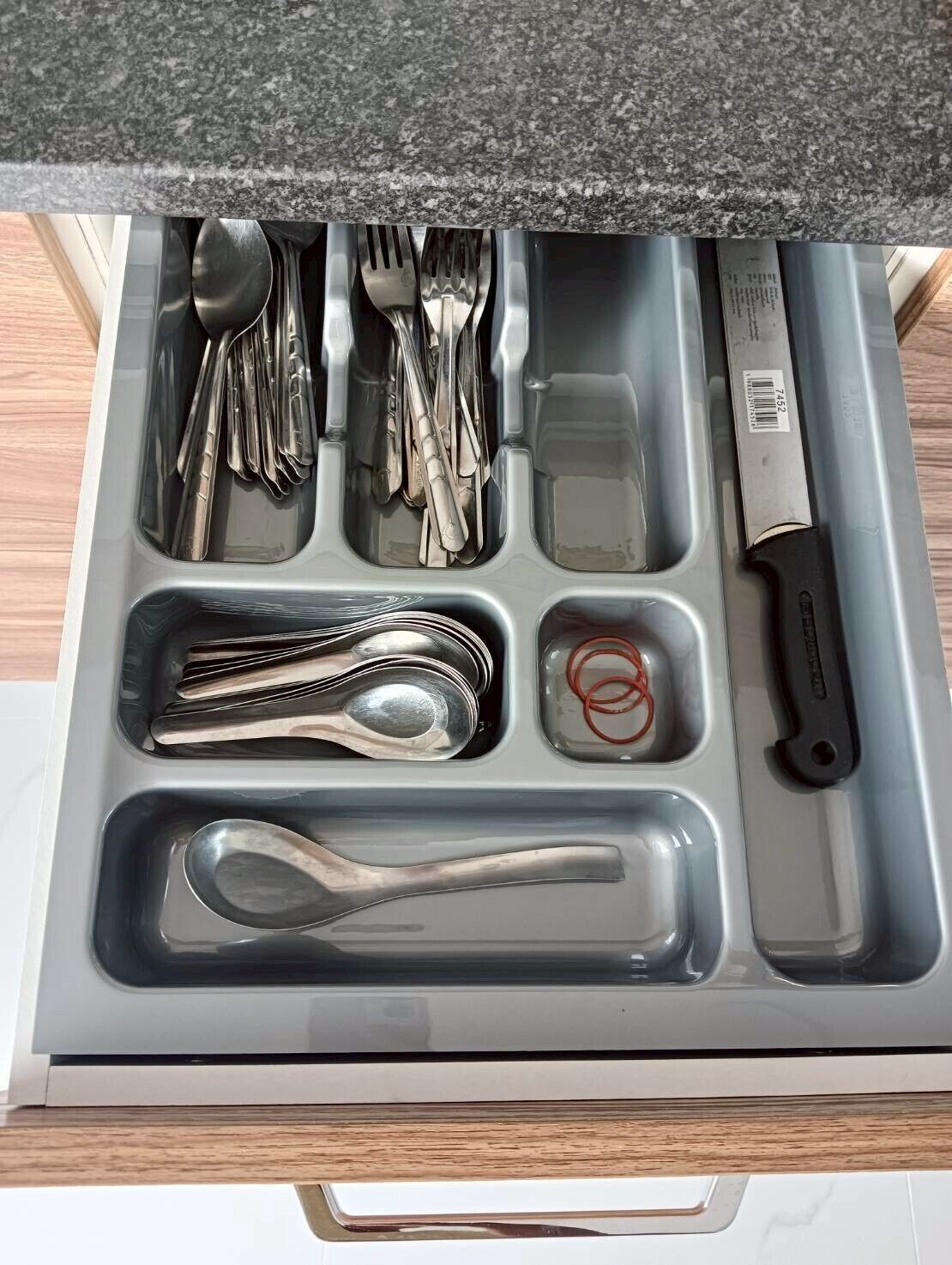 Un cajón con compartimentos que guardan diversos utensilios de cocina, como cucharas, tenedores, cuchillos y una tabla de cortar.