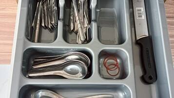 Un cajón con compartimentos que guardan diversos utensilios de cocina, como cucharas, tenedores, cuchillos y una tabla de cortar.