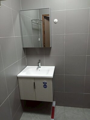 Une salle de bain avec un lavabo blanc, un miroir au-dessus, et une porte donnant sur une autre pièce.