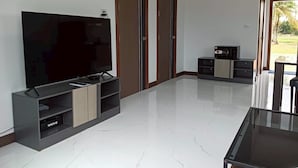 Un salon moderne doté d’un grand téléviseur à écran plat, d’une table basse en verre et d’un meuble TV avec espace de rangement.