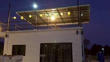 A modern building with a flat roof, large windows, and a covered outdoor area with hanging lights.