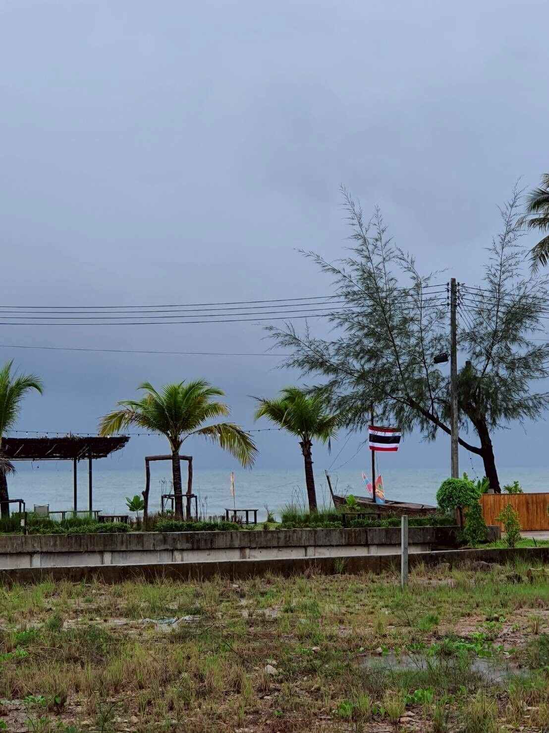 A coastal area with a concrete barrier, palm trees, and a flagpole with a flag.