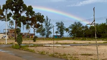 Una carretera pavimentada con césped y árboles, cielo despejado y un arcoíris a lo lejos.