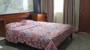 A bedroom with a bed, a wooden dresser, a marble wall, a window with curtains, and a door. - Charming 2BR duplex house rooftop Oasis (Colombo)