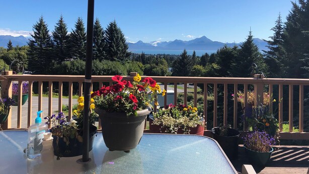 Un balcon agrémenté d’un parasol rouge, de plantes en pot et offrant une vue sur des montagnes et un lac.