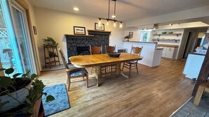Un vaste espace dédié à la salle à manger, avec une table et des chaises en bois, une cheminée en pierre et une cuisine en arrière-plan.