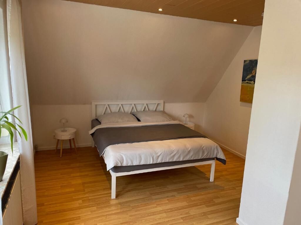A bedroom with a bed, a bedside table, a small round table, and a potted plant.