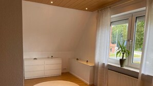 Un dormitorio con una ventana grande, un tapete redondo, una cama, un aparador y un radiador.