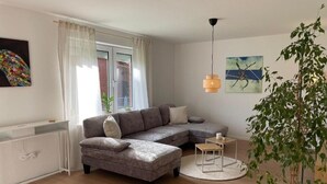 Una sala de estar moderna con un sofá seccional gris, una mesa de centro redonda, una planta en maceta y obras de arte en las paredes.