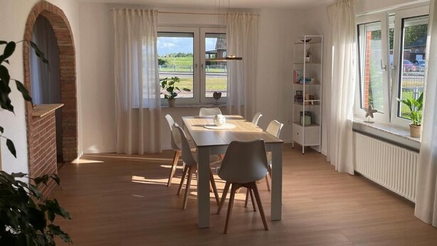 Un comedor con mesa y sillas de madera, una estantería y vistas al exterior.
