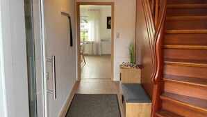 Un pasillo con escalera de madera, puerta de cristal y un banco.