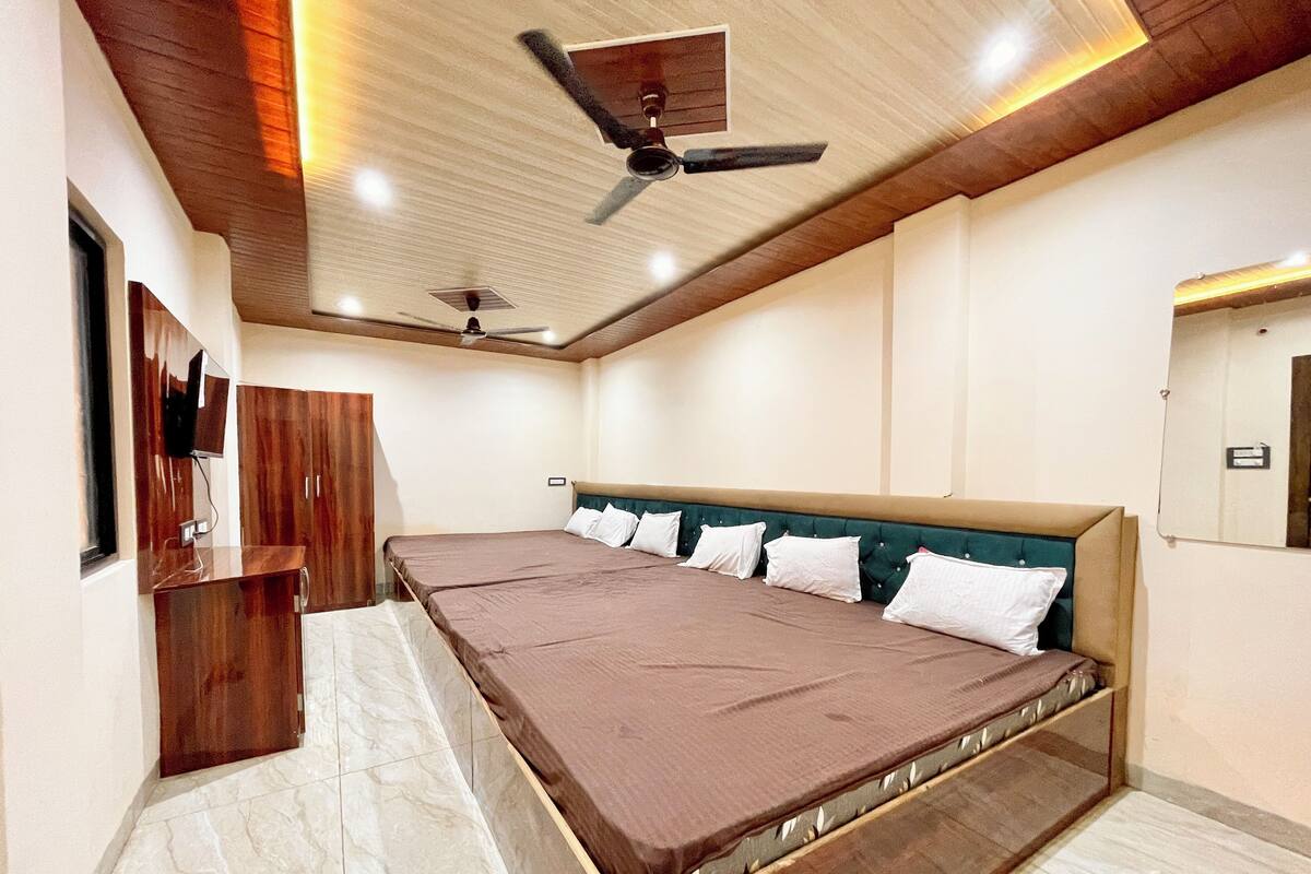 A bedroom with a large bed, wooden wardrobe, ceiling fan, and a mirror on the wall.