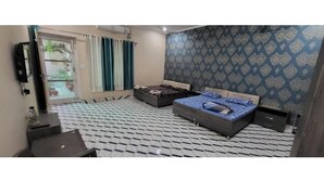 A bedroom with two beds, a TV, and a patterned wall. - Saini Guest House (Gurdaspur)