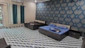A bedroom with two beds, a TV, and a patterned wall. - Saini Guest House (Gurdaspur)