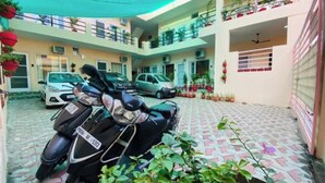A multi-story building with a covered parking area, potted plants, and a motorcycle. - Saini Guest House (Gurdaspur)