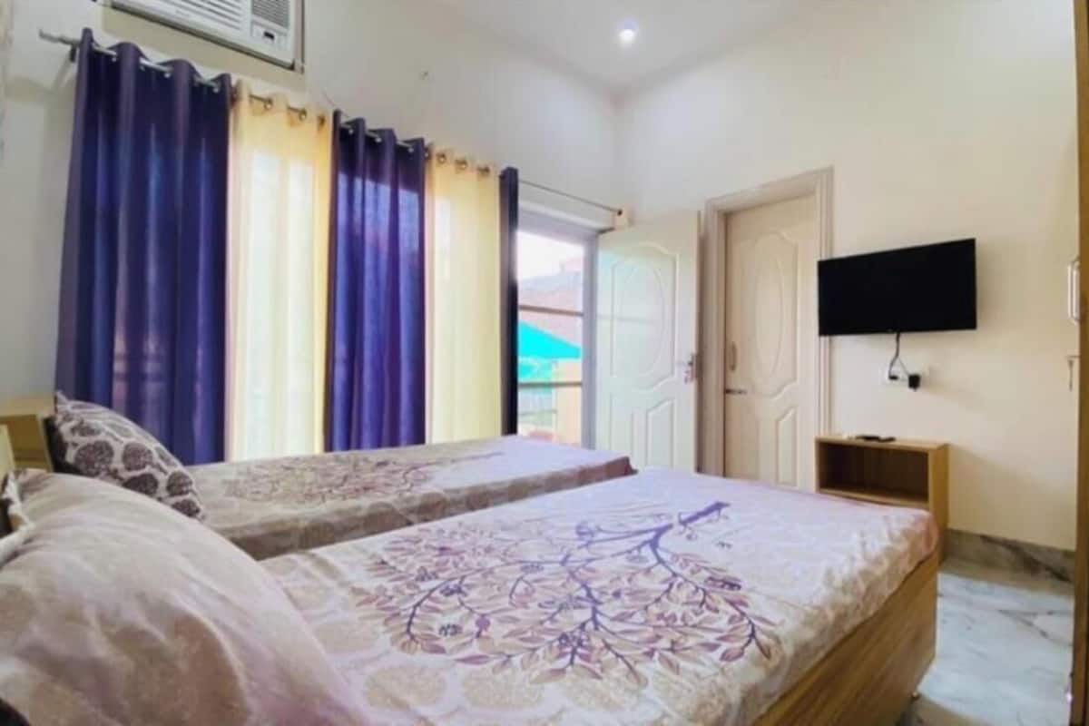 A bedroom with two beds, a TV mounted on the wall, and a door leading to an outdoor area.