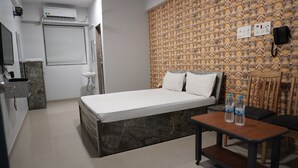 Habitación de hotel con cama, una mesita con botellas de agua, una silla, teléfono montado en la pared y aire acondicionado mural.