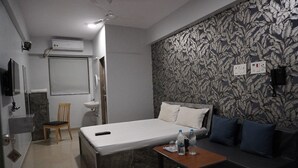Habitación de hotel con cama, sofá, mesita, silla, lavamanos y espejo.