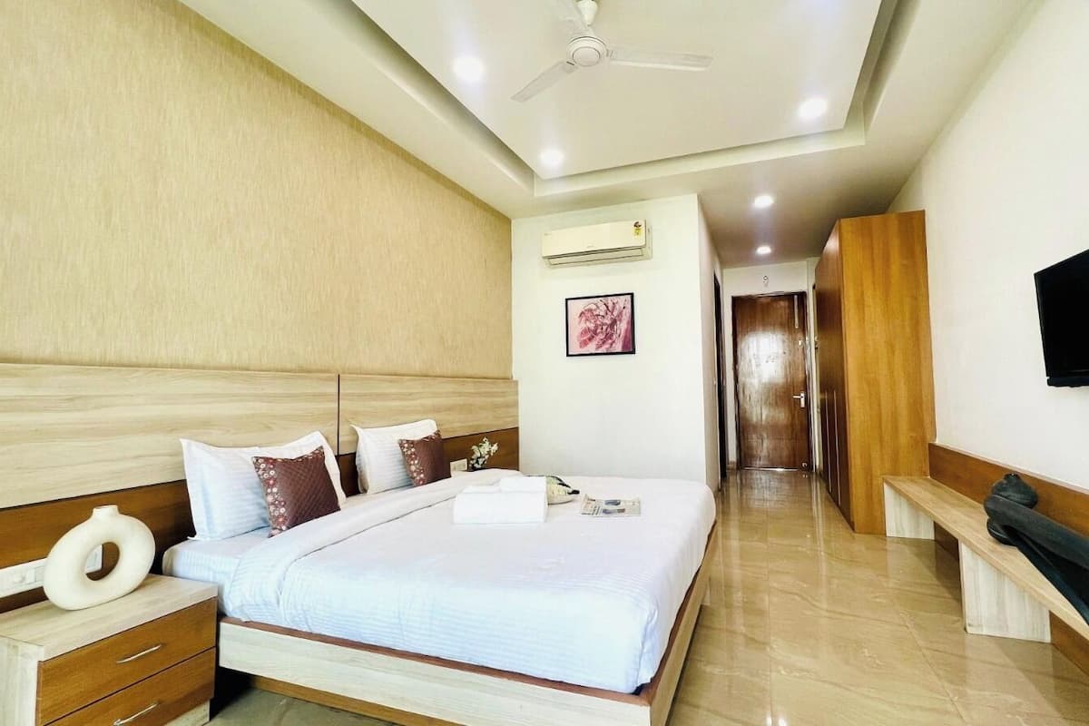 A modern hotel room with a large bed, wooden headboard, a flat-screen TV, an air conditioning unit, and a bench by the window.