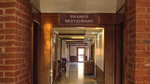 Un pasillo que conduce a un restaurante llamado 'BHANGO RESTAURANT', con paredes de ladrillo y puertas de madera.