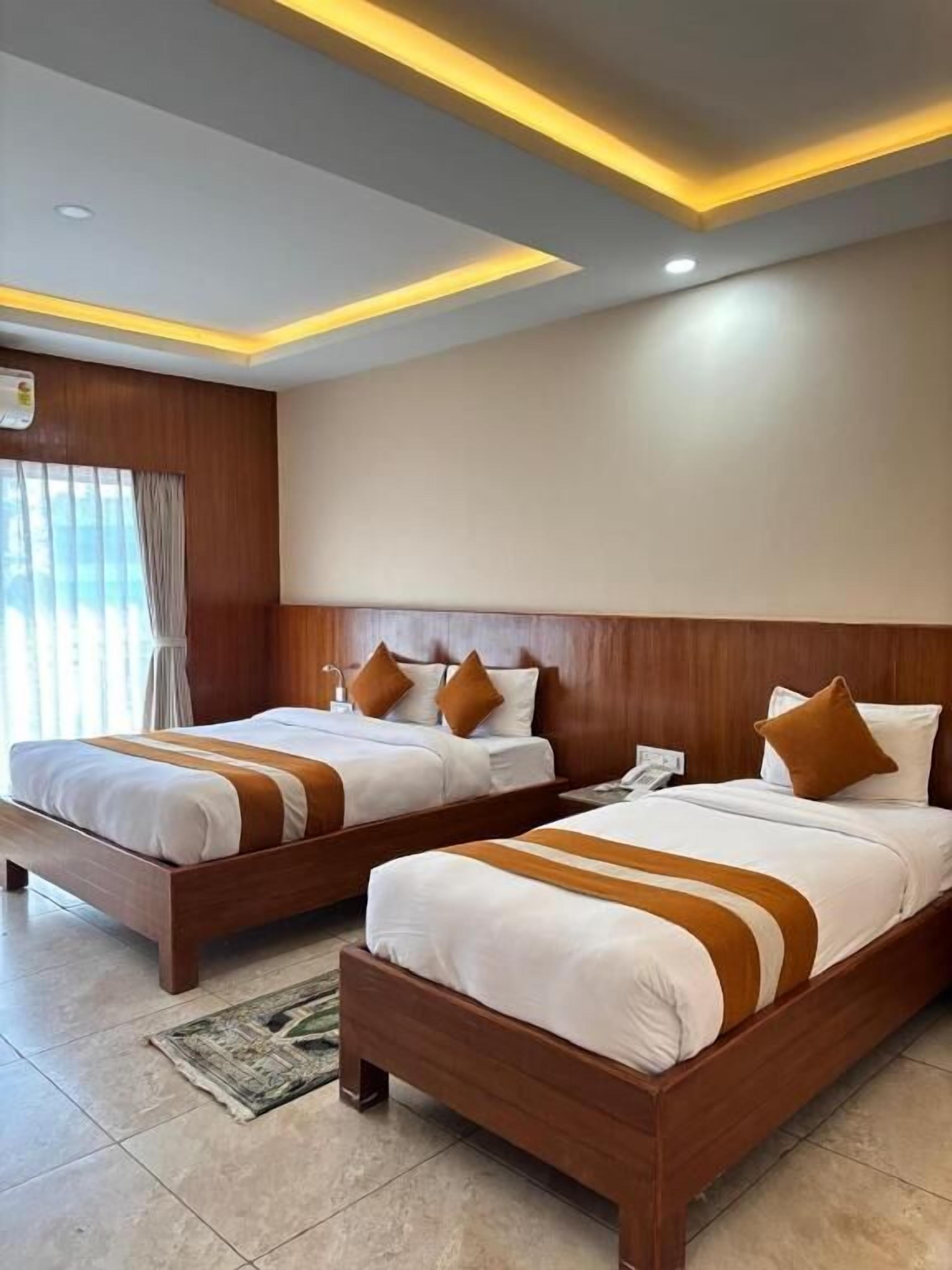 Quarto de hotel com duas camas de madeira, uma janela grande com cortinas e um design moderno no teto.