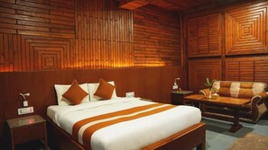 Une chambre d’hôtel avec un mur décoré de panneaux en bois, un lit avec une literie blanche et des touches de couleur orange, une table basse en bois et un canapé en cuir.