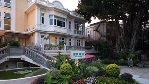 Un hotel de estilo arquitectónico tradicional, con un pequeño elemento acuático y una variedad de plantas y flores en el jardín.