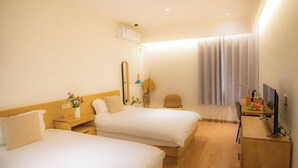 Habitación de hotel con dos camas, un escritorio con silla, televisor y una ventana con cortinas.