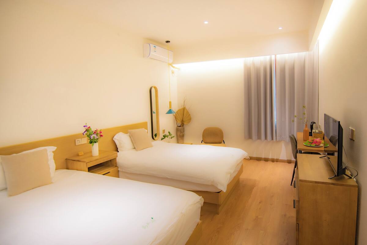 A hotel room with two beds, a desk with a chair, a television, and a window with curtains.