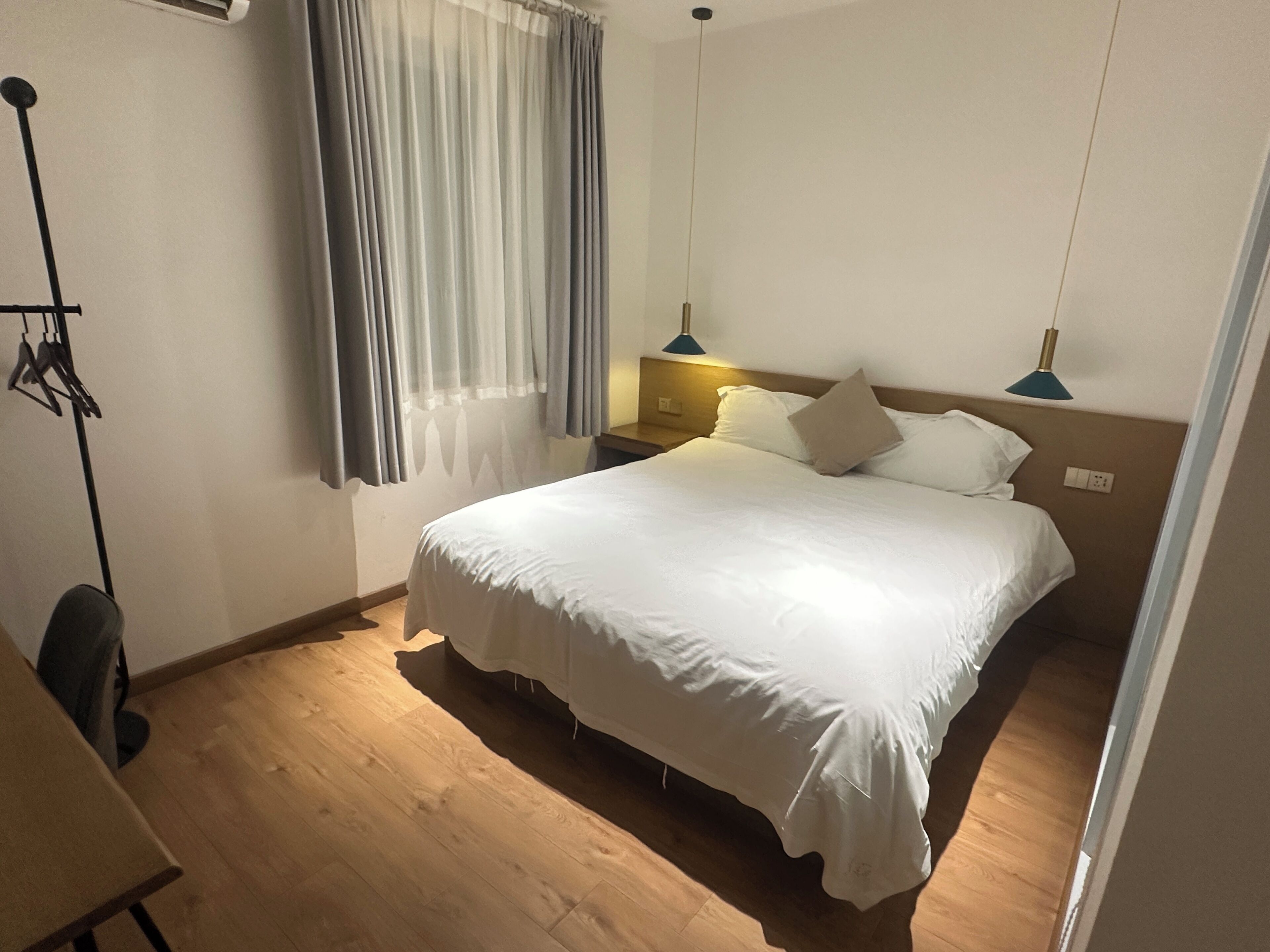 Una habitación de hotel con una cama grande, un escritorio y una silla. Hay dos lámparas de noche y una ventana con cortinas.