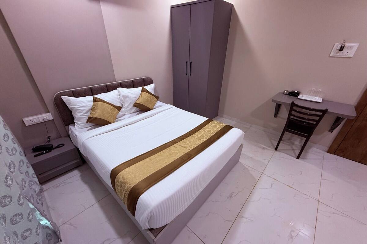 Habitación de hotel ordenada con cama, armario, escritorio pequeño y una silla.