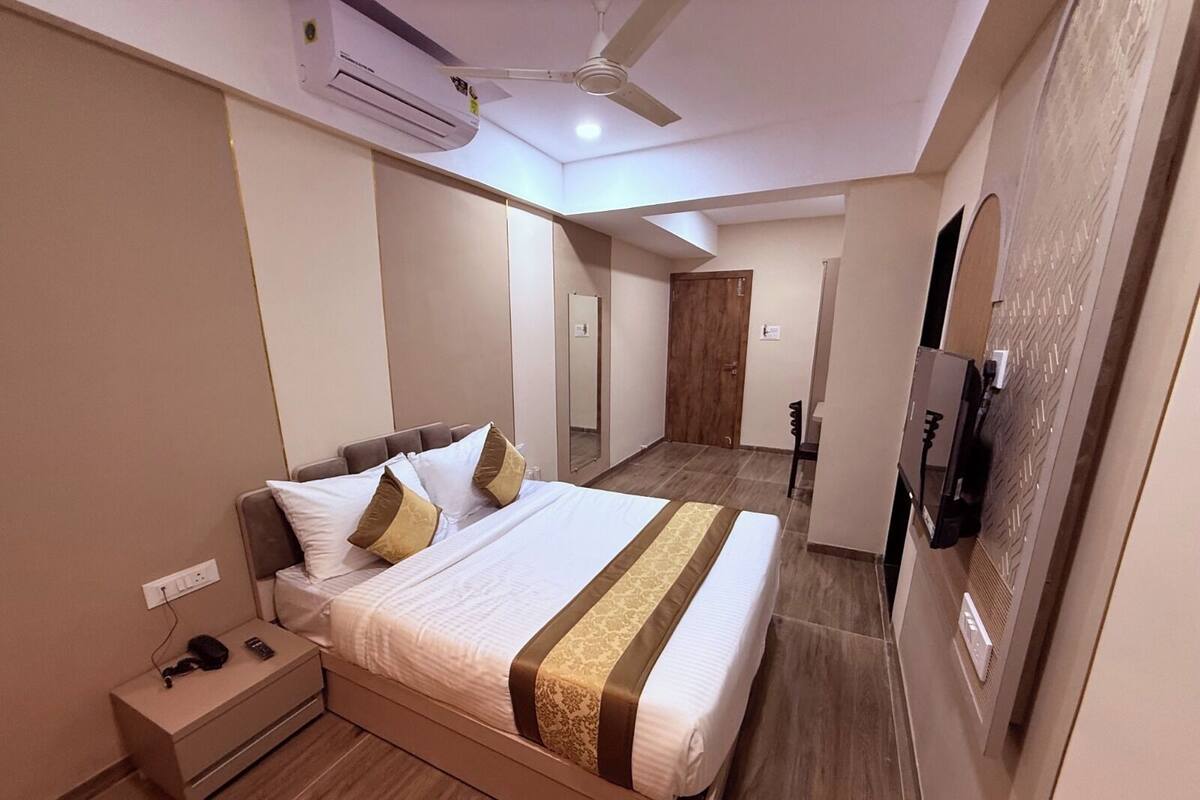 Habitación de hotel con cama, mesita de noche, aire acondicionado, ventilador de techo y televisor montado en la pared.