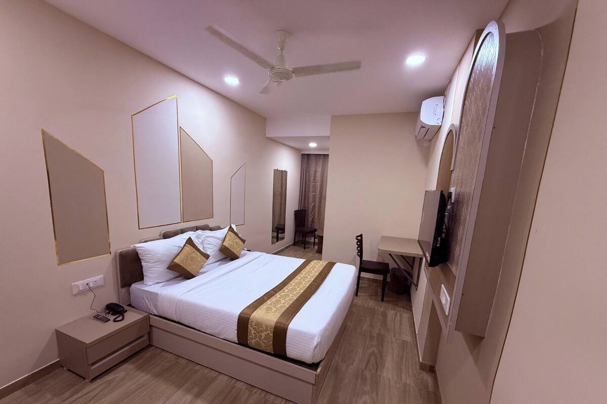 Una habitación de hotel con cama, mesita de noche, escritorio, silla y ventilador de techo.
