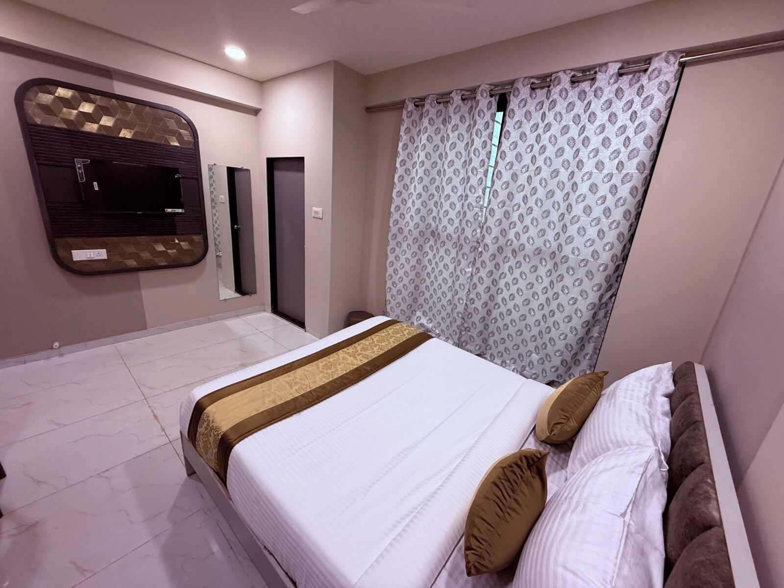 Quarto moderno com cama grande, espelho e cortina estampada.