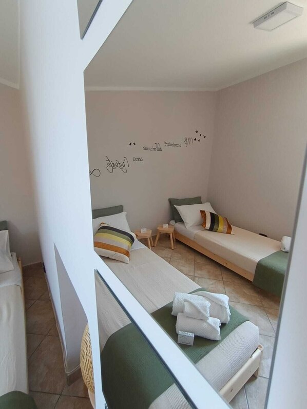 A small, well-lit room with two single beds, a small table, and a wall with decorative text.