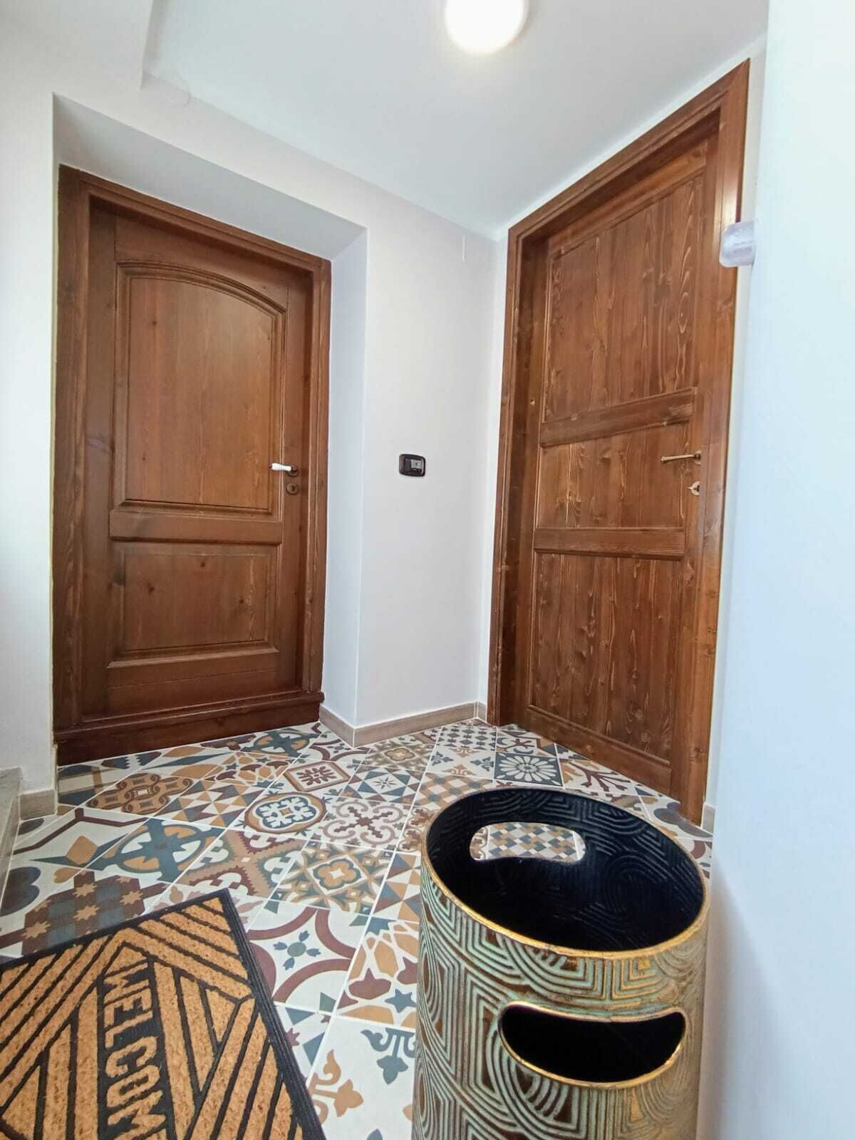 Een hal met twee houten deuren, vloertegels met een patroon en een decoratieve mand.