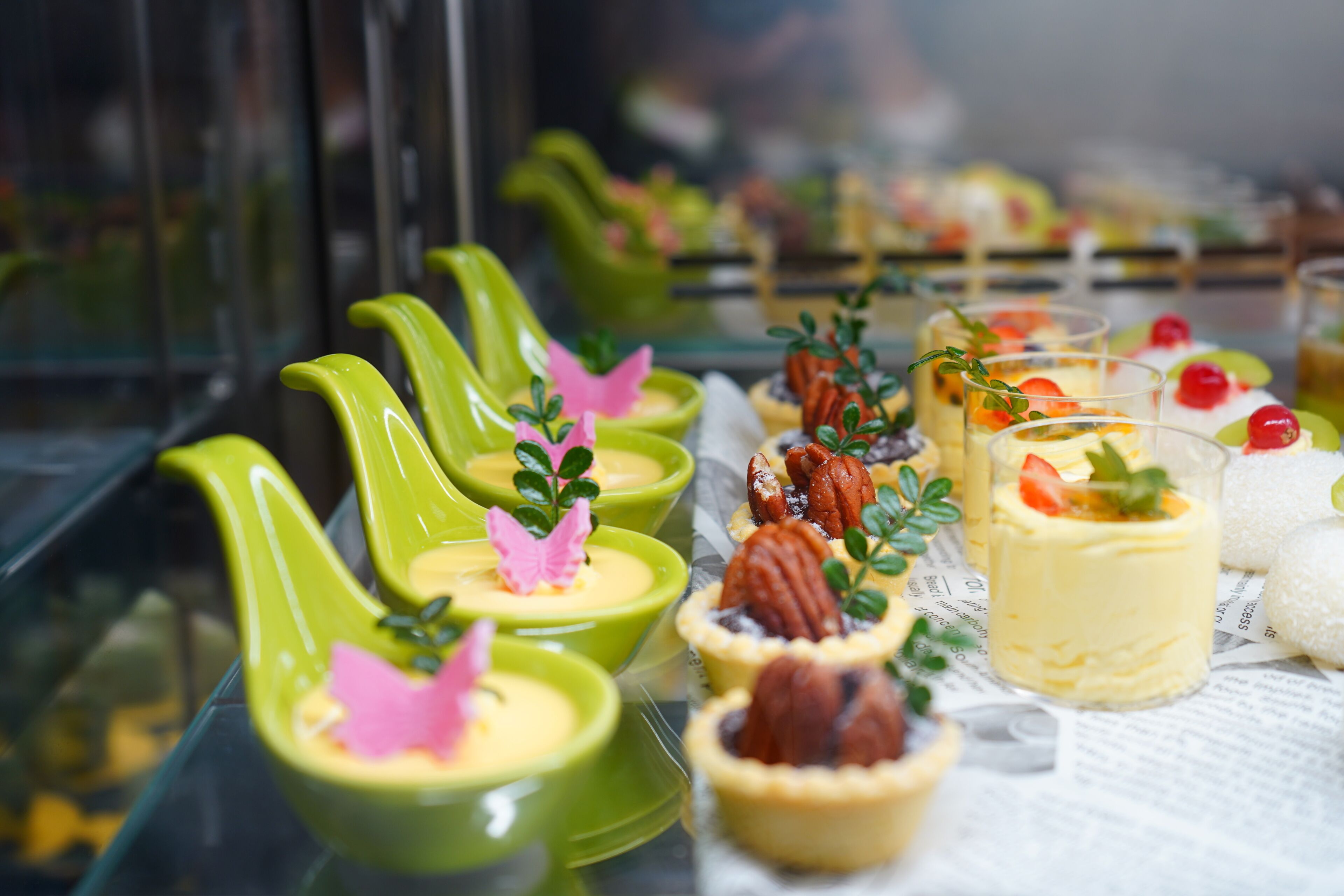 A variety of desserts displayed in green ceramic cups and glasses, some with decorative elements like berries and leaves.