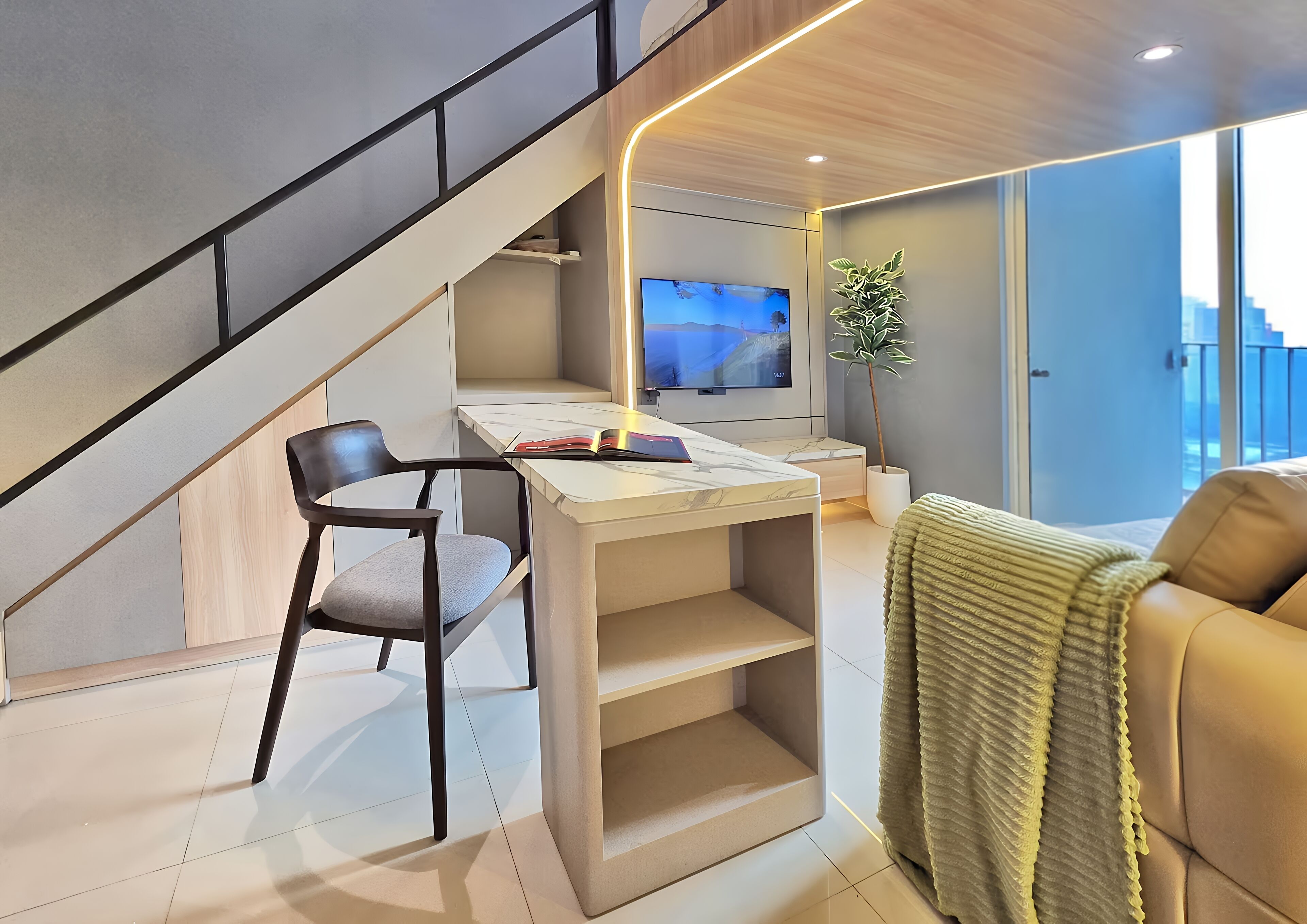 A modern living room with a staircase, a flat-screen TV, a desk with a chair, and a sofa.