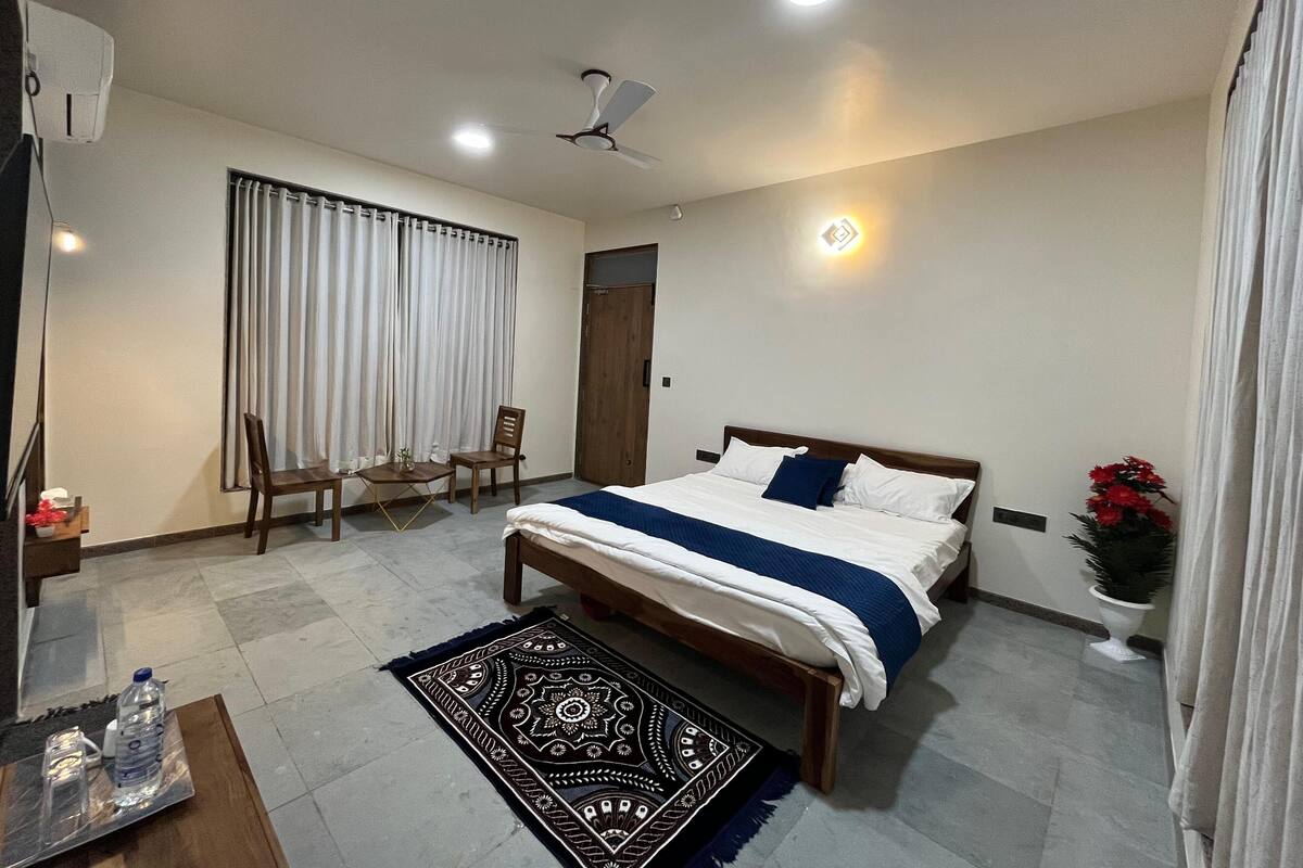 Quarto com cama, escrivaninha, cadeiras, ventilador de teto e um vaso de planta.