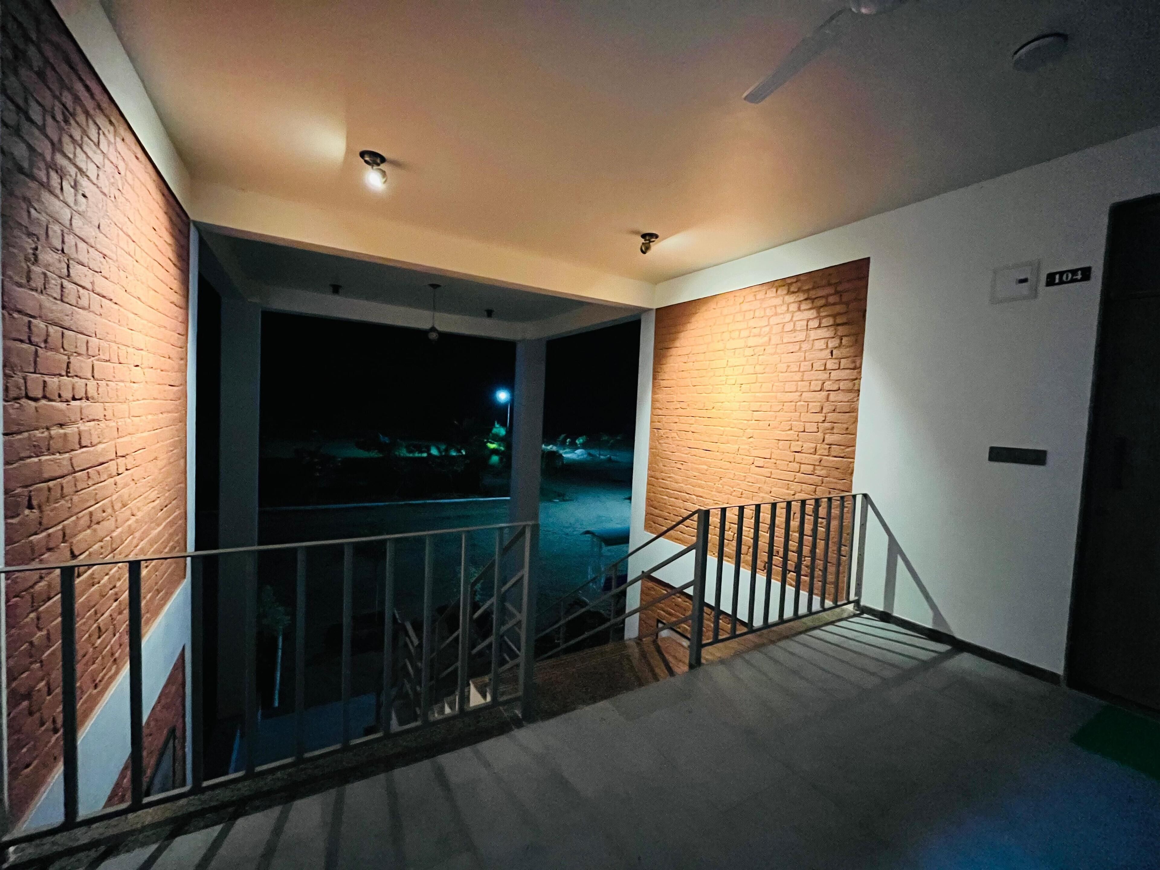 Una escalera conduce a un balcón con un muro de ladrillo en un lado y una puerta marcada con el número 104 en el otro.