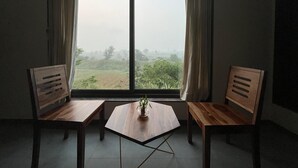 Una habitació amb un gran finestral, dues cadires de fusta, una taula petita i una planta en test.